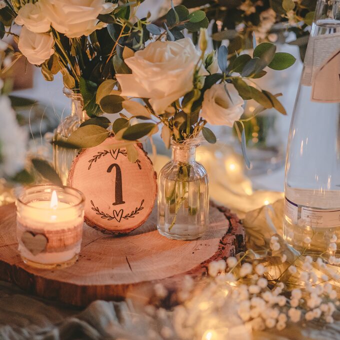 Tischdekoration mit Kerze, Tischnummer auf einer Holzscheibe und weißen Rosen