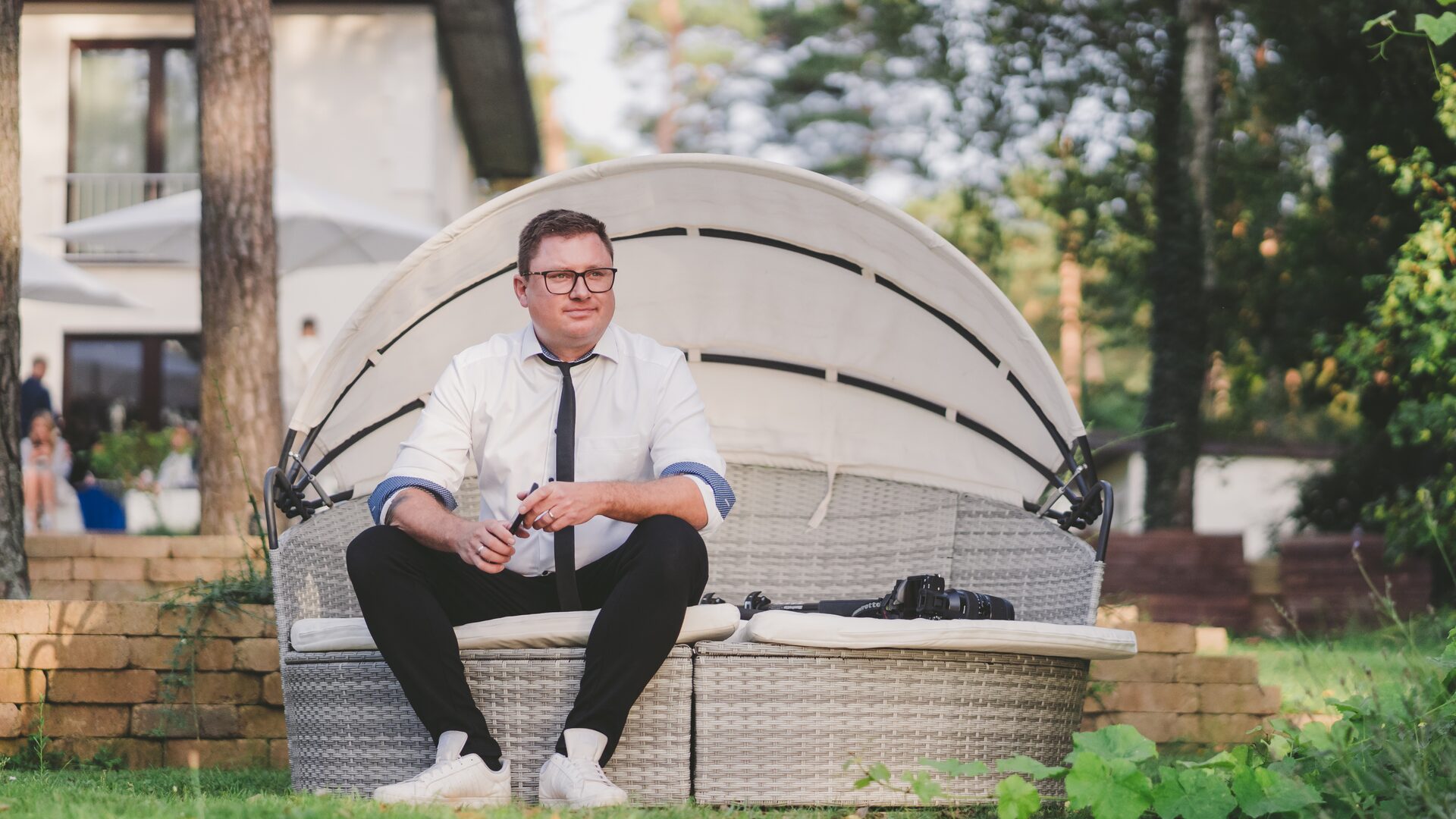 Der Fotograf sitzt mit seiner Kamera auf einem Gartensofa im Grünen
