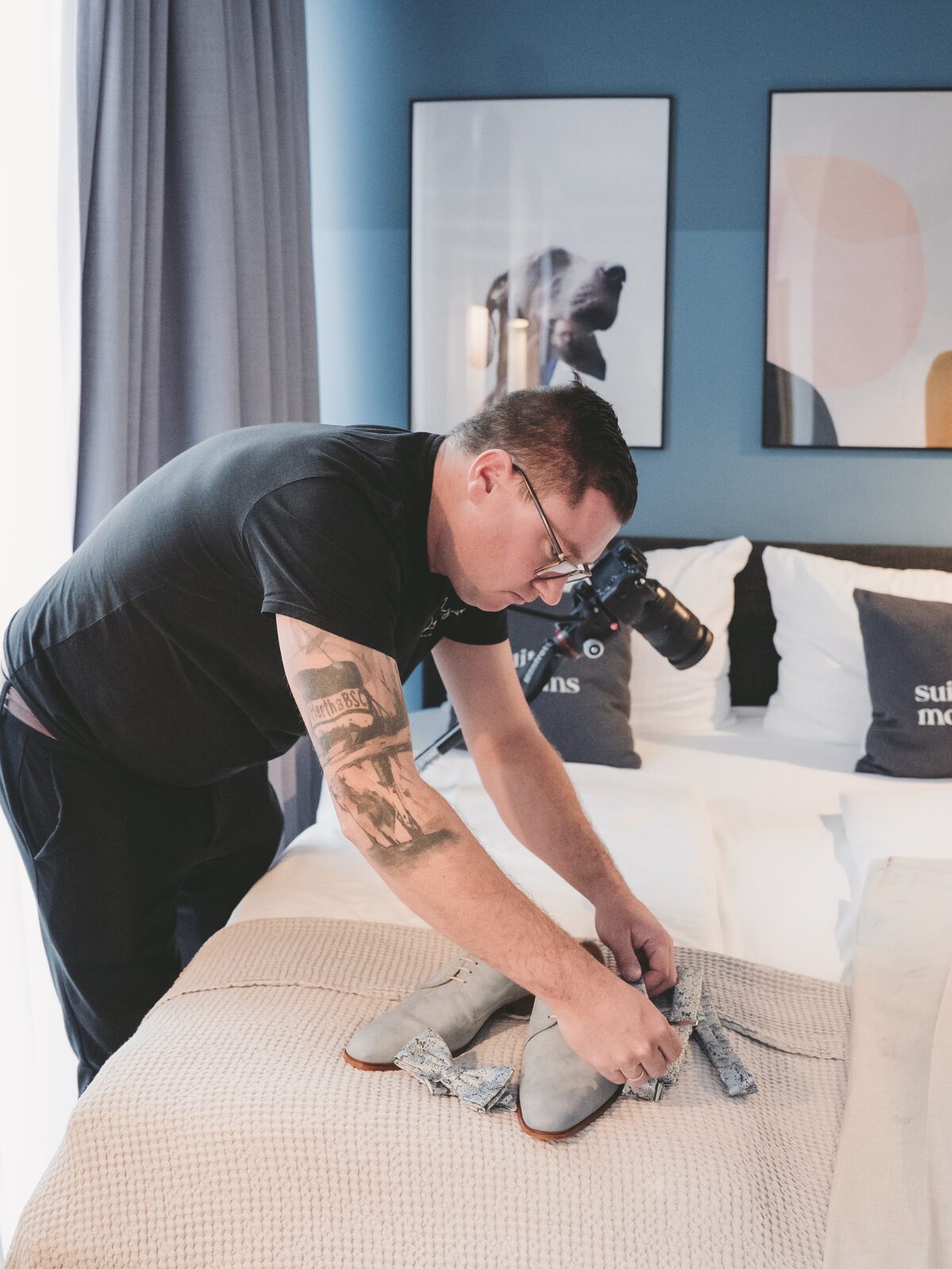 Fotograf mit Kamera legt im Hotelzimmer die Schuhe der Braut auf dem Bett zurecht